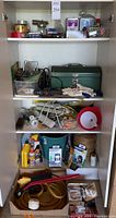 Shelving unit containing assorted hardware items such as tapes, work gloves, metal toolbox, hand tools, shop light, and other accessories.