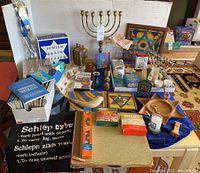 Photo showing various Judaica items including brass Menorah, framed Jewish star, Machzor books, plastic Shofar, Purim items, and various candles among other items.