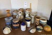Overview image showing all 18 pottery pieces including vases, containers, paperweights, wood vase and jewelry boxes on brown surface.