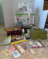 Brother ES-2000 sewing machine on carpet with original box behind, assorted sewing supplies and vintage green metal storage box in foreground.