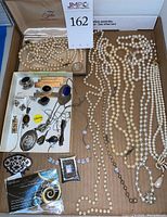 Top down view of box containing multiple cultured pearl necklaces, several sterling silver rings, earrings, and pendants with various stones including onyx and lapis lazuli