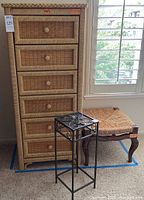 Tall wicker dresser with 6 drawers next to wicker and wood bench and small metal table.