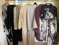 Group view of 8 women's coats and jackets on hangers showing various styles and materials including wool cape and leather jacket