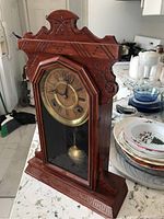Side view of the wooden mantel clock showing the carved decoration, glass door, and pendulum inside