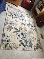 Full shot of the rectangular floral patterned area rug on light carpet flooring, showing overall design and condition.