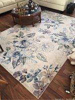 Angle showing the full floral patterned rug placed in a living room with furniture around it, highlighting the pattern and colors.