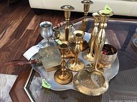 View of brass candlesticks, wooden-handled silent butler, teapot, ashtray, pewter cup, and aluminum tray on wooden floor.