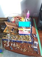 Overview photo showing three containers and various costume jewelry items including pins, brooches, and necklaces laid out on a table.