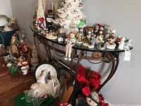 Demilune shaped wrought iron frame table with beveled glass top shown with various decorative holiday items placed on and under the table.