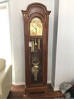 Full front view of oak grandfather clock showing arched top, clock face, pendulum and weights