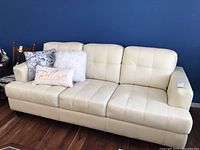 Front view of cream leather couch with three throw pillows against a blue wall