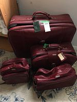 Photo showing all four pieces of burgundy Samsonite luggage together on a carpeted floor, with tags attached.