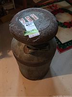 Top and side view of vintage metal milk can showing latch mechanism on the lid and embossed number 79 on the body, surface covered with rust and patina.