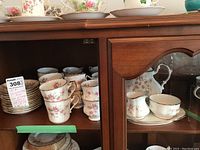 Assorted cups, saucers and service pieces displayed on a cabinet shelf