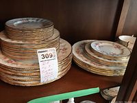 Stacks of dinner, salad and bread plates in cabinet showing white china with pink rose pattern and gilt scalloped edges.