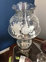 Glass parlor lamp with white flower designs on ruffled top glass shade, brass base visible.