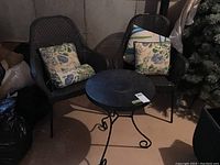 Full view of two dark brown cane armchairs with floral cushions and one black round metal side table in a basement setting