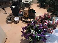 Wide view showing multiple planter pots, a lantern, metal stand, and faux flowers in purple and pink with greenery.