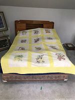 Full view of the bed quilt spread on a bed, showing yellow borders and the arrangement of floral embroidered blocks with month names.