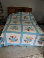 Full view of quilt spread over bed showing multiple Dresden Plate pattern squares with light blue sashing and white background.