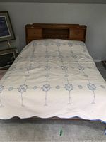 Full view of the quilt bed cover on a bed showing cream base color with blue embroidered pattern in grid layout.