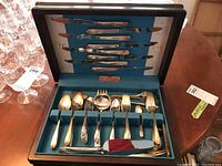 Photo of complete flatware set stored in original blue lined wooden box, showing a wide assortment of knives, forks, and spoons.