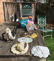 Full lot view showing leaf blower, lawn chairs, solar stake lights, and garden decor arranged on a wooden picnic table with grass and fence background.