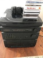 Front view of Magnavox compact stereo system stacked with over-ear headset on top and a stack of music CDs including Beatles and Johnny Cash beside headset.