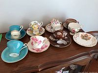 Seven sets of teacups and saucers of varying colors and patterns displayed on wooden surface