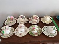 Eight vintage fine bone china teacup and saucer sets arranged on wooden surface showing different floral patterns and styles