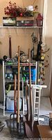 Long view of yard tools and items arranged on wire shelving rack including rakes, shovels, pitchfork, pet bowls, garden chemicals, decorative items like wind chimes and floral arrangements.