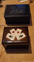 Photo showing two decorative wooden boxes, one dark with carved patterns and one lighter polished with playing card suit decorations on lid.