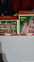 Two boxes of Lemax lighted Christmas houses displayed side by side, showing box art and branding.
