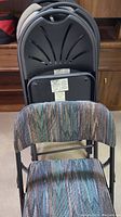 Seven folding chairs stacked, showing striped multicolor fabric padded chair front with black metal frame and decorative cutout backrest.