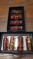 Box with 8 glass cutlery rests showing colorful patterns embedded inside each rectangular piece.