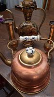 Photo showing copper kettle with ceramic handle, brass lid, and part of brass ewer and vases