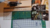 Overview of all items in the mat cutting lot including the ruler, green cutting mat, mat cutter, and the instruction book.