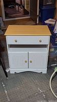 Full front view of small white wooden cabinet with natural wood top showing drawer, open shelf, and double-door storage.
