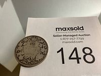 Canadian 50 cents coin showing the reverse side with the date 1917 and maple leaf motif, placed next to a maxsold auction label with lot number 148