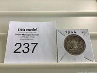 Photo of the coin in protective holder alongside auction lot card 237