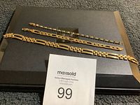 Three costume bracelets displayed on a black surface including two gold-tone bracelet chains and one rhinestone bracelet with green and clear stones.