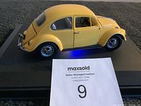 Side view of yellow Franklin Mint 1967 Volkswagen Beetle model car on black display base from left side.