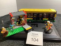 LEGO green and yellow bus, bus stop, and minifigures arranged on black display