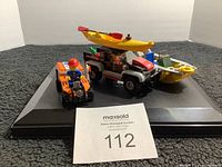 Photo showing a Lego lot on a black display stand with a multi-colored vehicle, yellow kayak on top, an orange ATV, and a minifigure seated on the ATV.