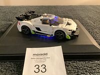 Side view of white and black Lego racing car with blue under-car lights on display platform.