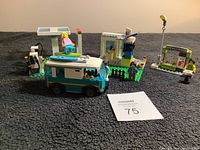 Overall view of Lego gas station set including camper van, gas station, newsstand, and figures placed on carpeted surface.