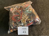 Plastic bag filled with assorted costume jewelry items on a dark carpet, showing colorful beads and metallic chains.