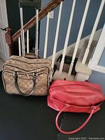 Photo shows brown rolling travel case with patterned fabric and large red leather textured carrying bag side by side.