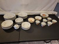 Overall view of two china sets with multiple plates, bowls, cups, and a sugar bowl laid on a black surface against a light backdrop.