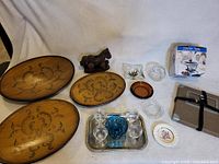 Photo showing all items: three wooden trays with designs, wooden horse figurine, two clear glass ashtrays, blue glass item, small ceramic dish, silver tray with clear glasses, and two plastic containers.